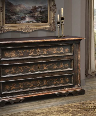 Cassettone con frontale dei cassetti decorati con fregio floreale, finitura di base in laccatura antica testa di moro e decoro in giallo ocra.