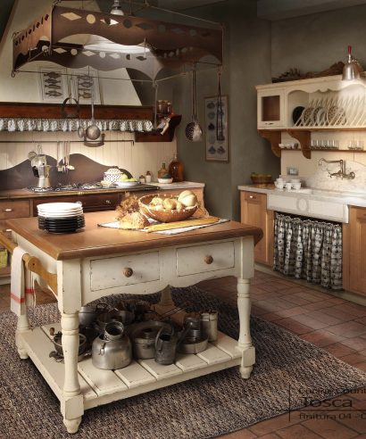 Cucina stile country in legno castagno, grande isola centrale con cassetti e attacca rame in ferro battuto.