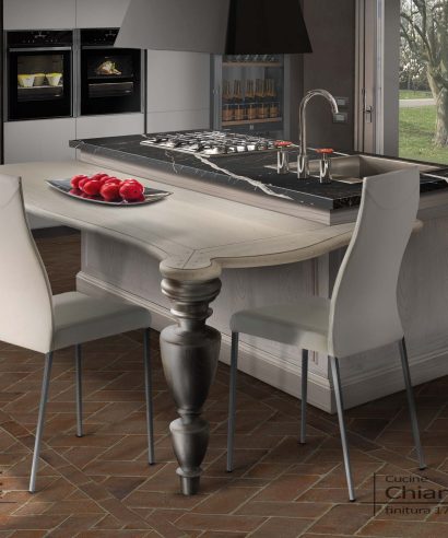 Cucina a isola centro stanza costruita in frassino, con piano di marmo nero Marquinia nella zona operativa della cottura e del lavello.