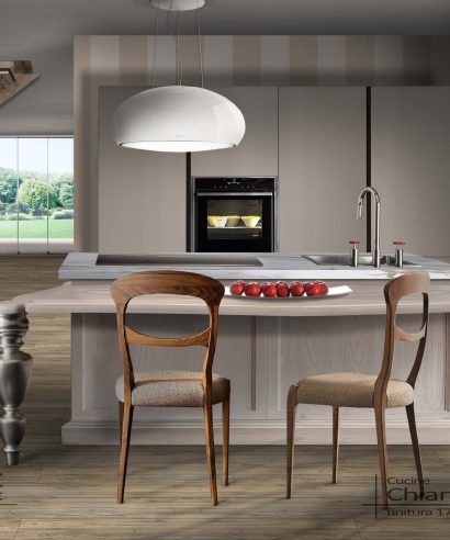 Ambiente cucina romantico e moderno con grande isola centro stanza con cottura e lavello e grande tavolo penisola con piano sagomato.