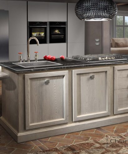 Cucina isola centro stanza con piano cottura e lavello, appendice grande tavolo penisola da pranzo.