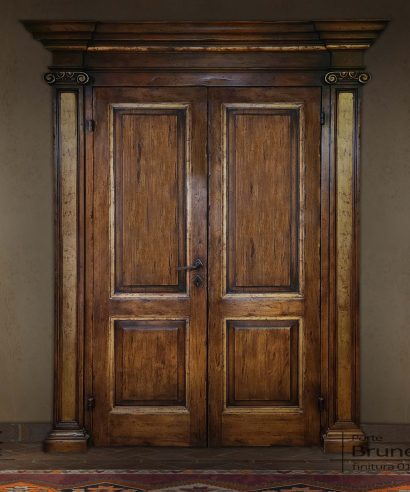 Porta rinascimentale a due battenti per interno, con portale in legno con colonne e capitelli intagliati a mano e grande cornice superiore.